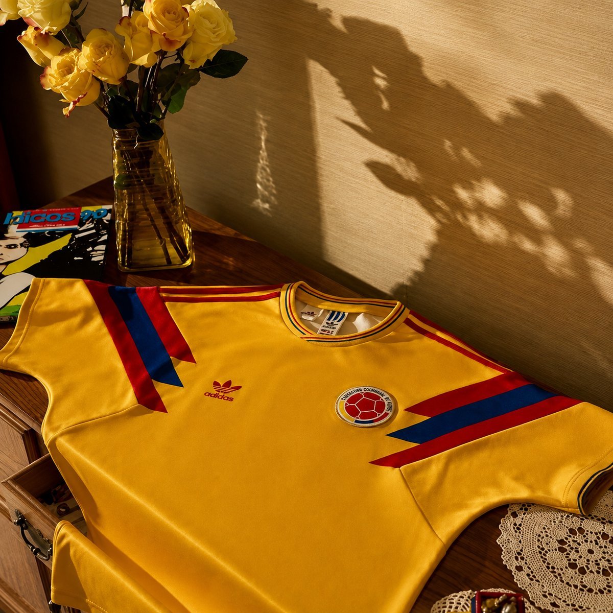 adidas 1990 Colombia retro shirt laid flat on a wooden surface, with FCF badge, red-blue chevron trim, 1990 World Cup era styling
