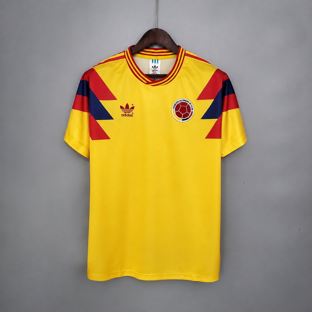 adidas 1990 Colombia World Cup retro shirt on a wooden hanger, with the Colombian Football Federation badge and red-blue diagonal stripes