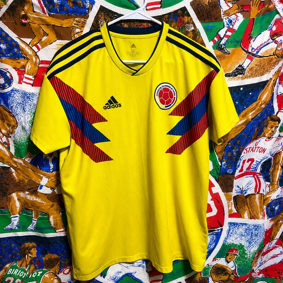 adidas 1990 Colombia World Cup retro shirt hung in front of a hand-painted World Cup mural, with the Colombian Football Federation badge and red-blue chevron detail